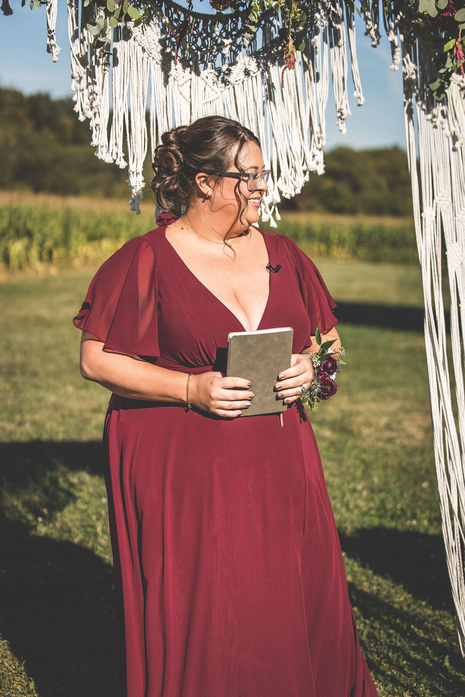 Wedding party members in burgundy dresses gather under a macrame backdrop outdoors.