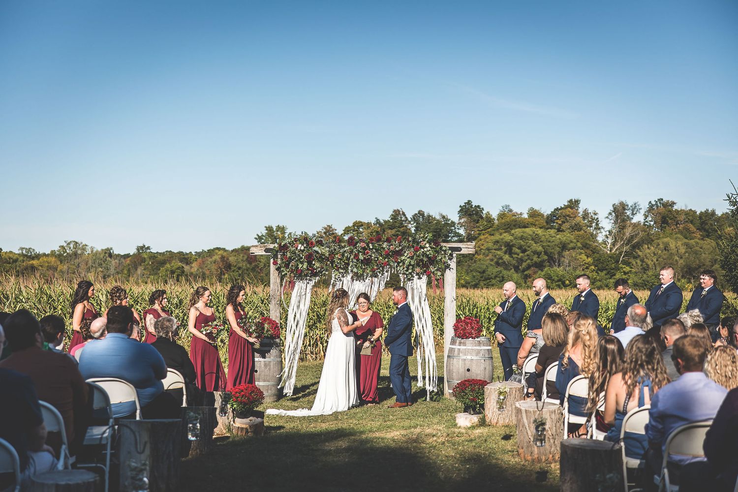 Panoramic view of outdoor wedding ceremony with guests seated on white chairs.