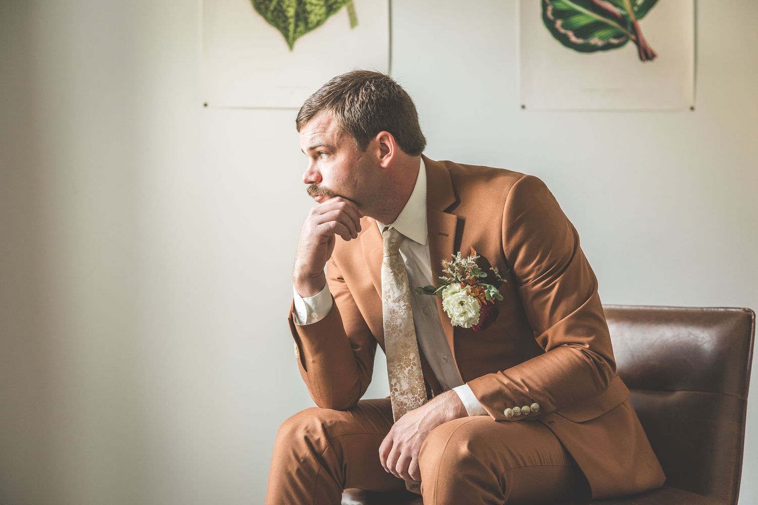 A person in a brown suit sits thoughtfully in a leather chair.