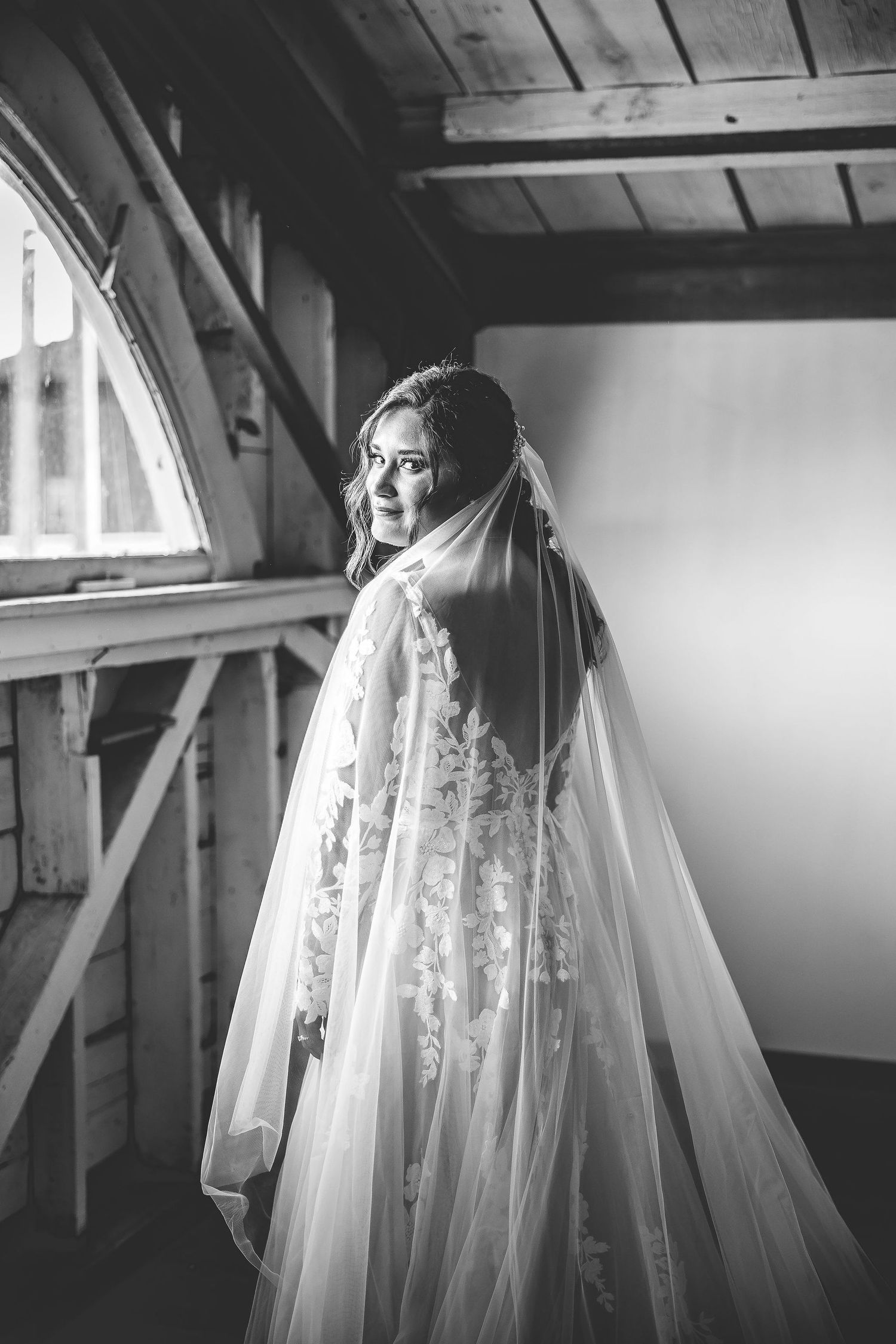 Dramatic black and white bridal portrait with flowing veil in natural window light.