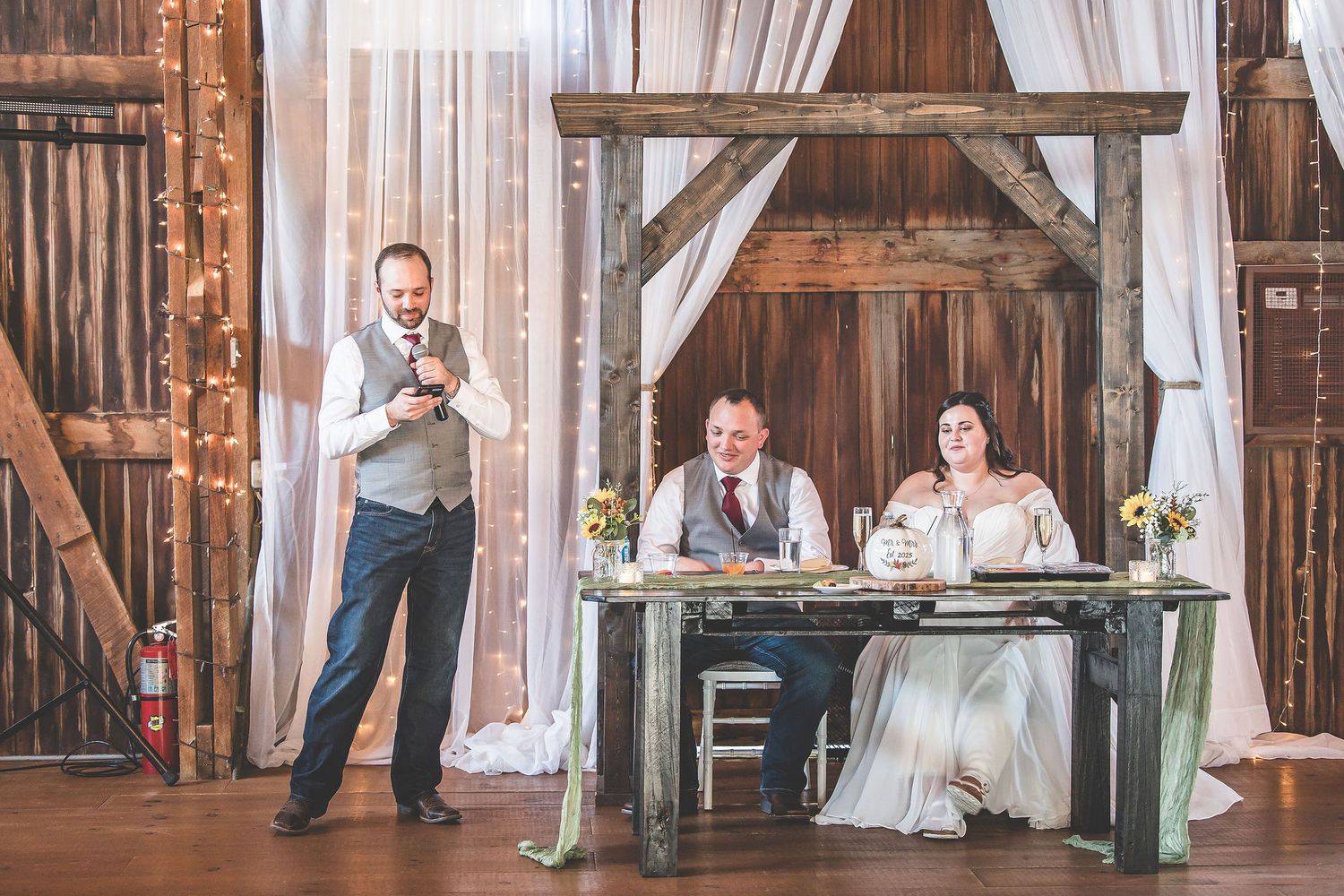 Wedding celebration in a barn venue with white curtains and wooden architectural details.