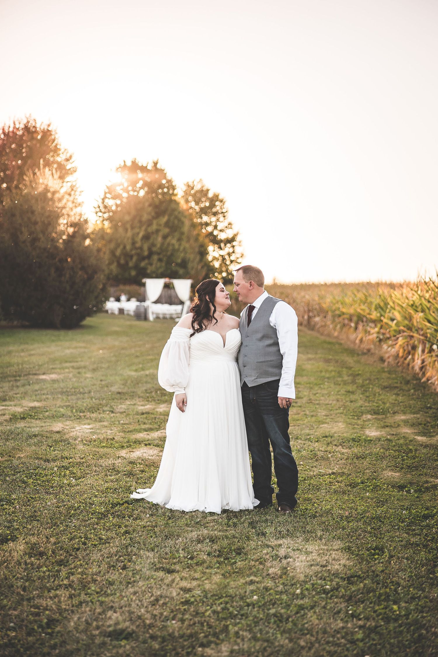 A couple shares a romantic sunset moment in a field near a cornfield.