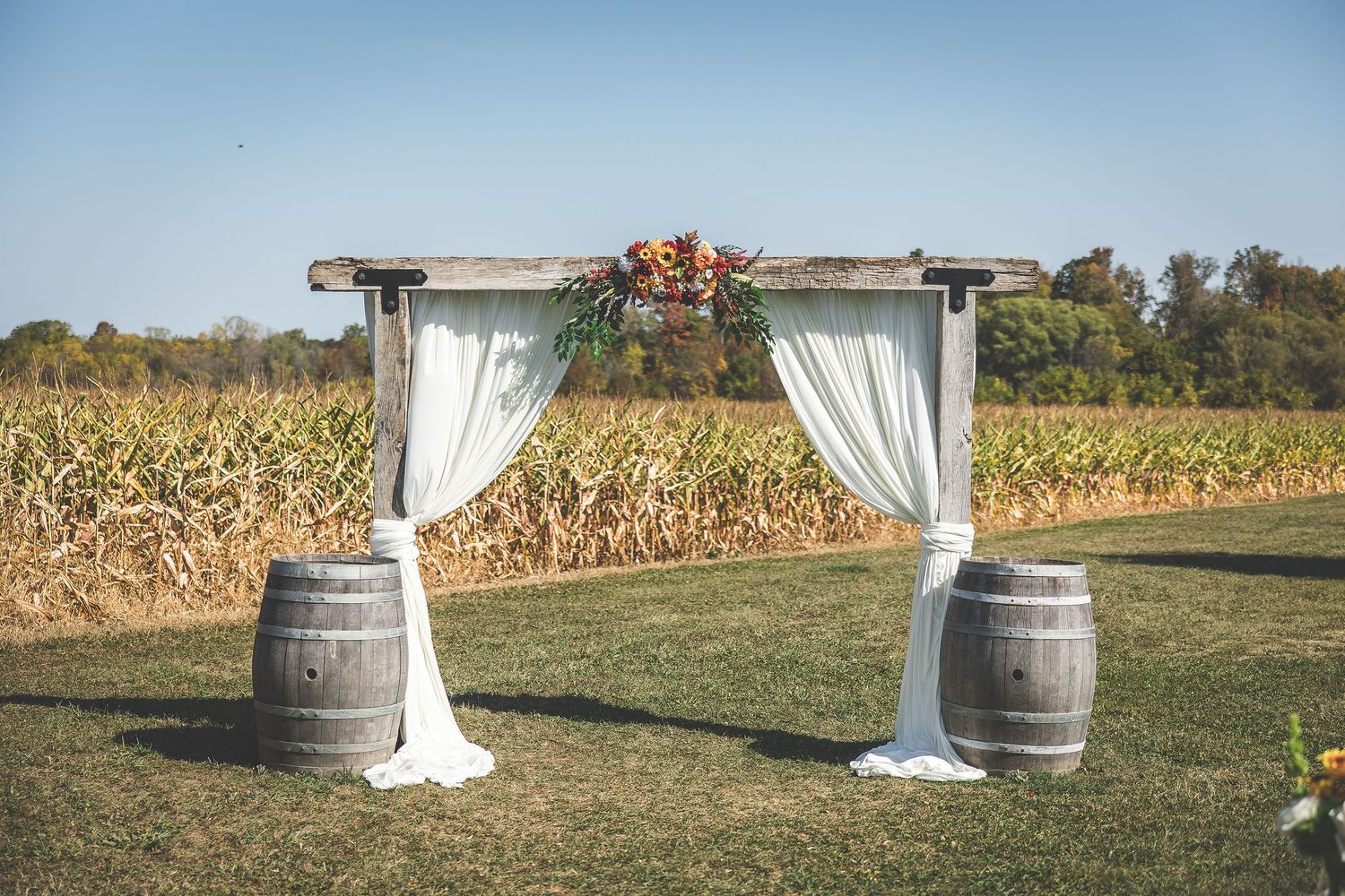 Outdoor wedding ceremony setup with white fabric draped arch and wine barrels.