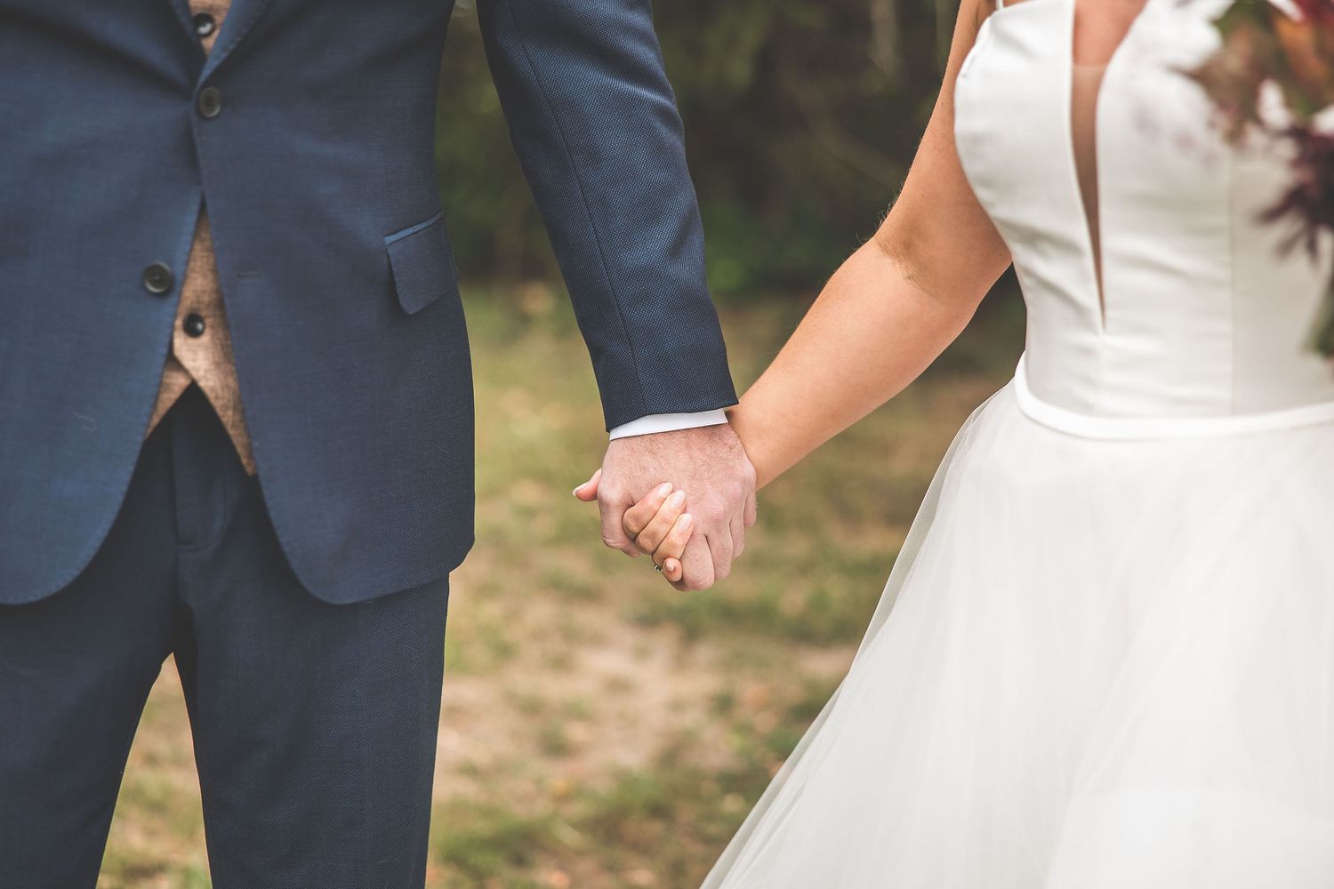 Bride in white dress and groom in navy suit pose with their dog during outdoor wedding.