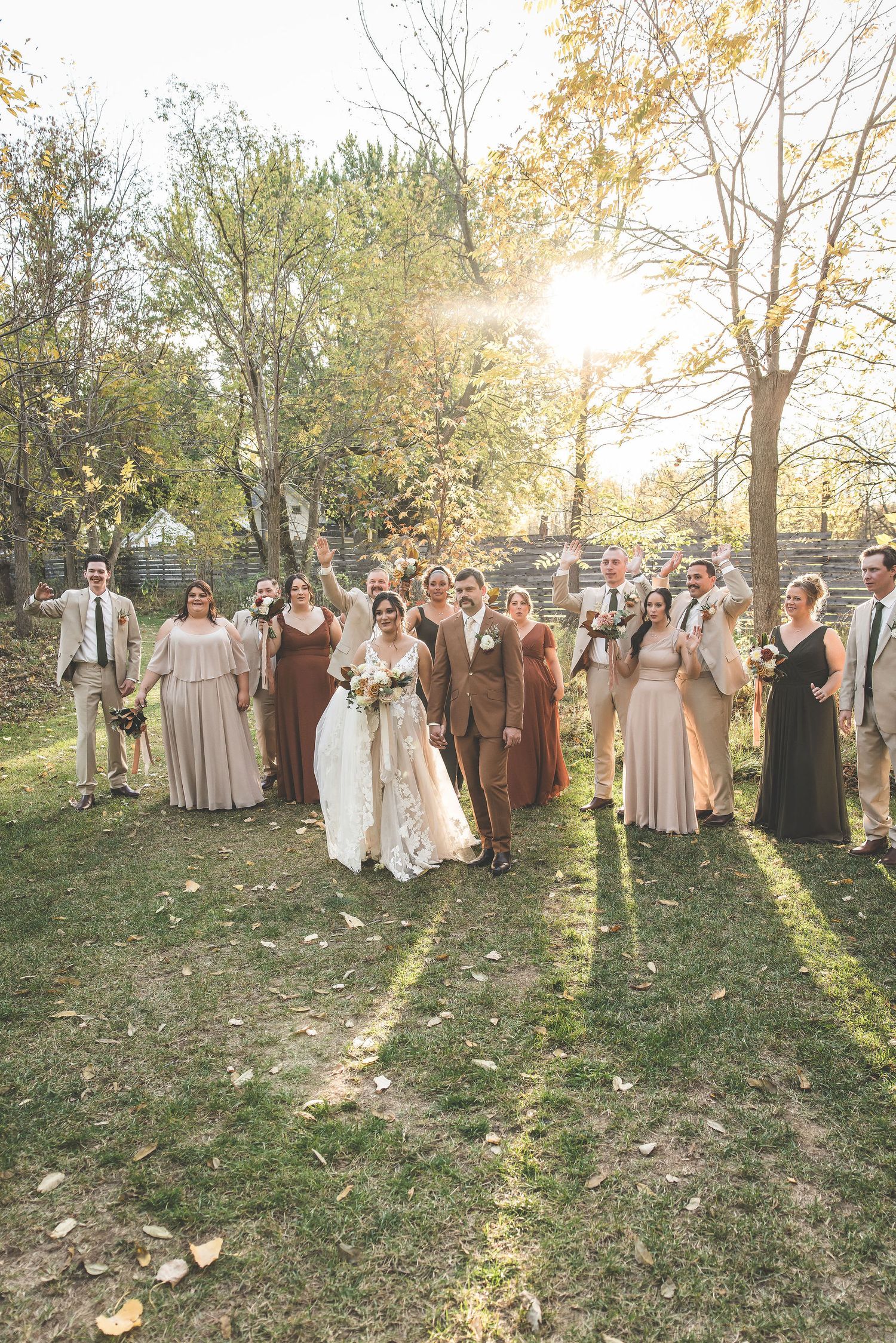 Wedding party gathered in outdoor autumn setting with sunlight streaming through trees.
