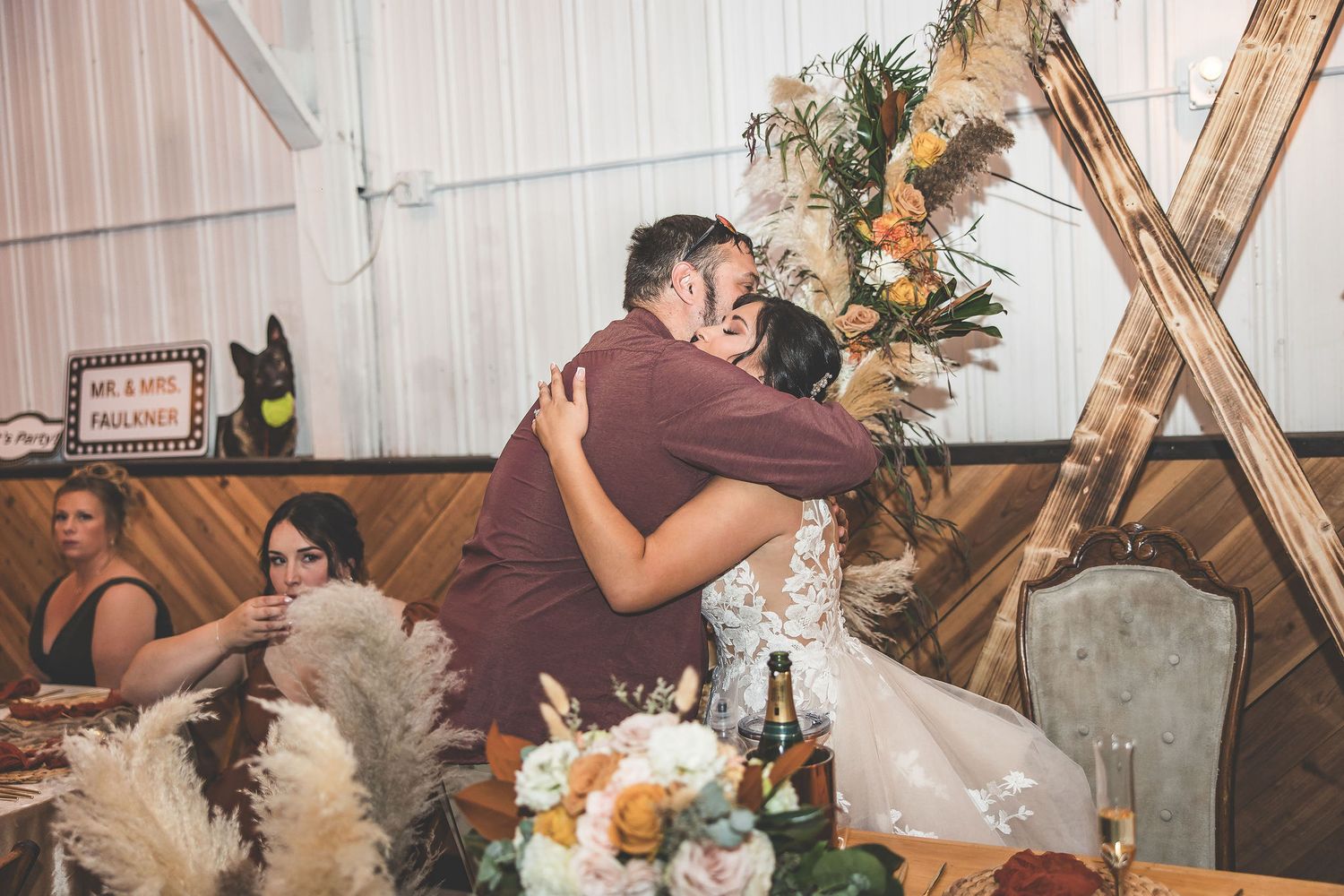 Wedding reception decor features rustic wooden accents and floral arrangements with pampas grass.