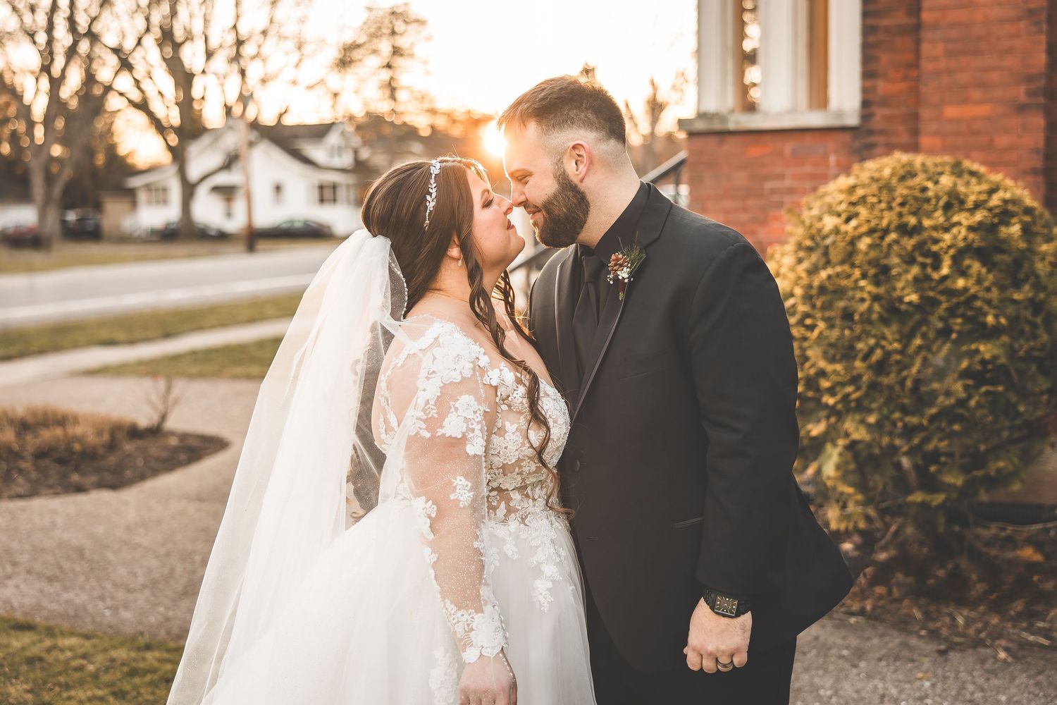 Romantic wedding couple shares intimate moment outside historic brick church at sunset.