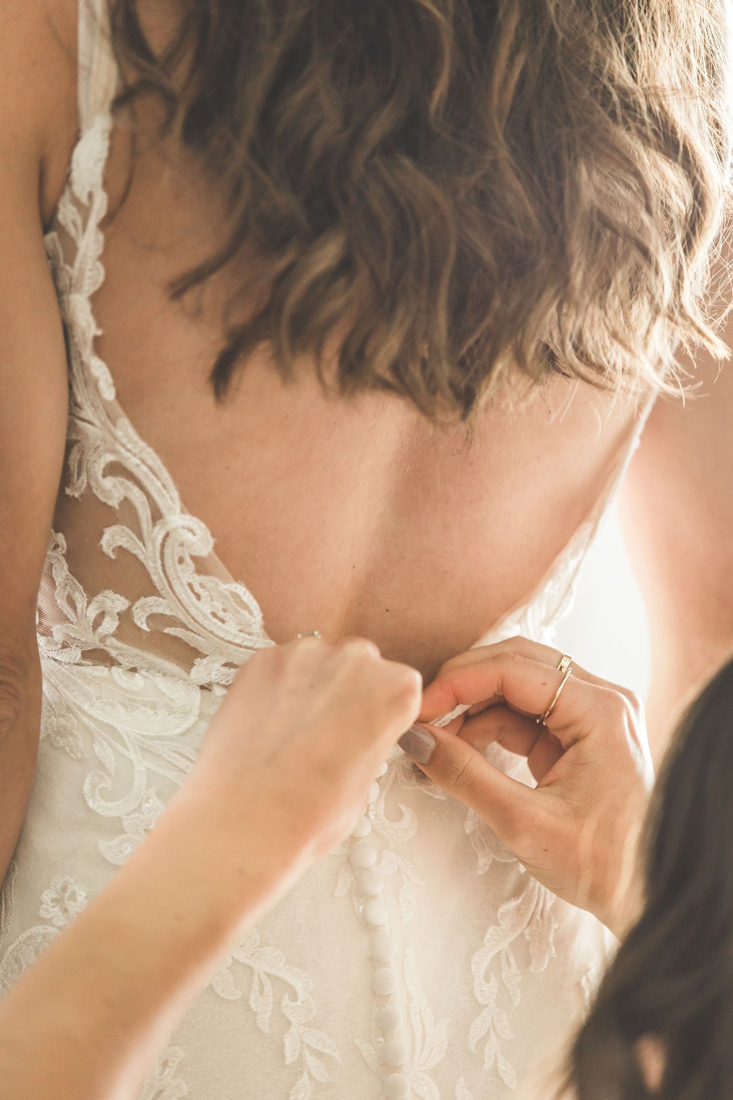 Close-up detail of lace buttons being fastened on a white wedding dress.