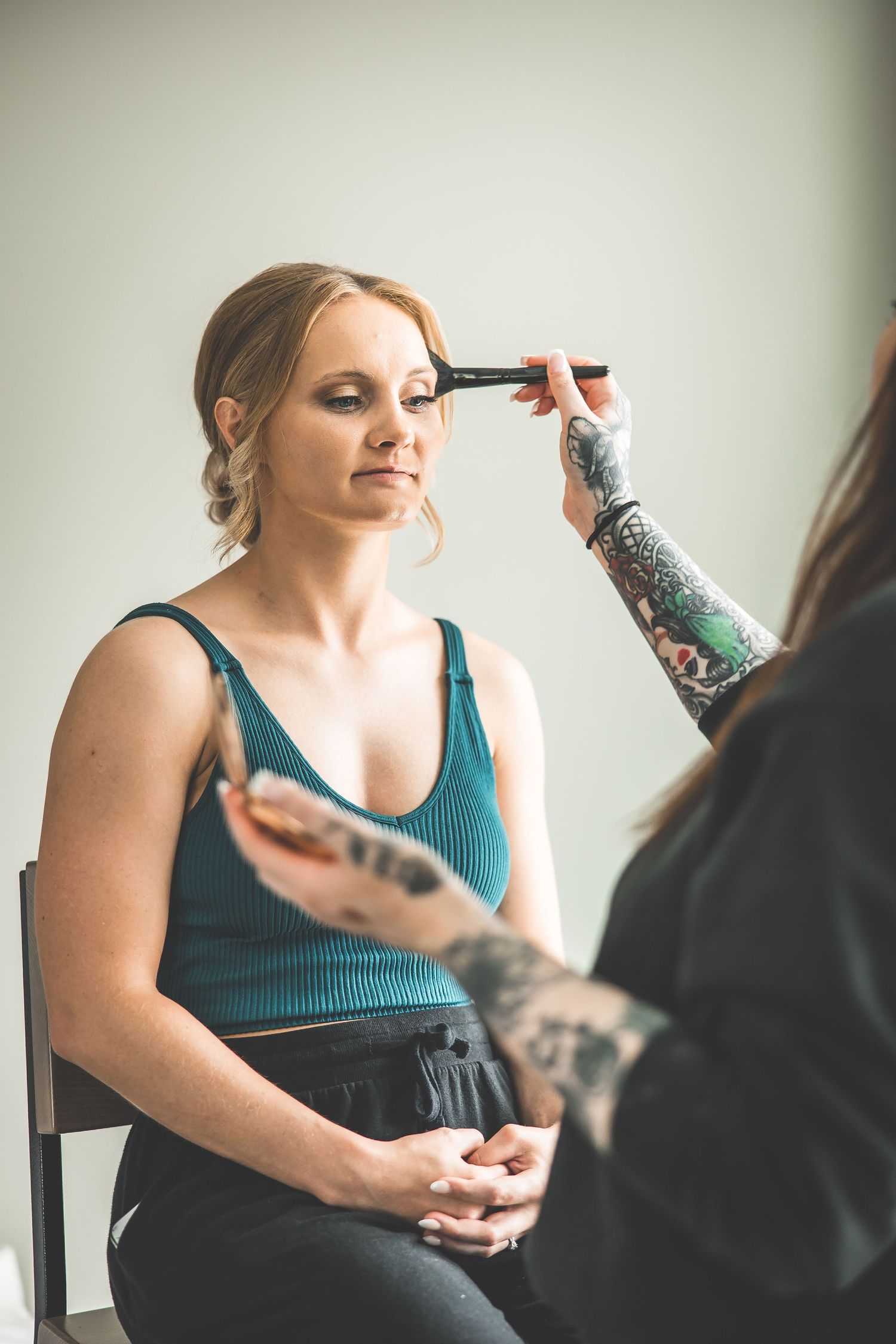 Bride getting makeup applied while wearing a teal top during wedding preparations.