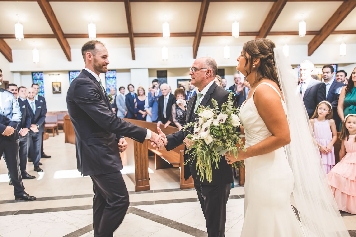 Wedding ceremony in progress at a bright church sanctuary with exposed wooden beams.