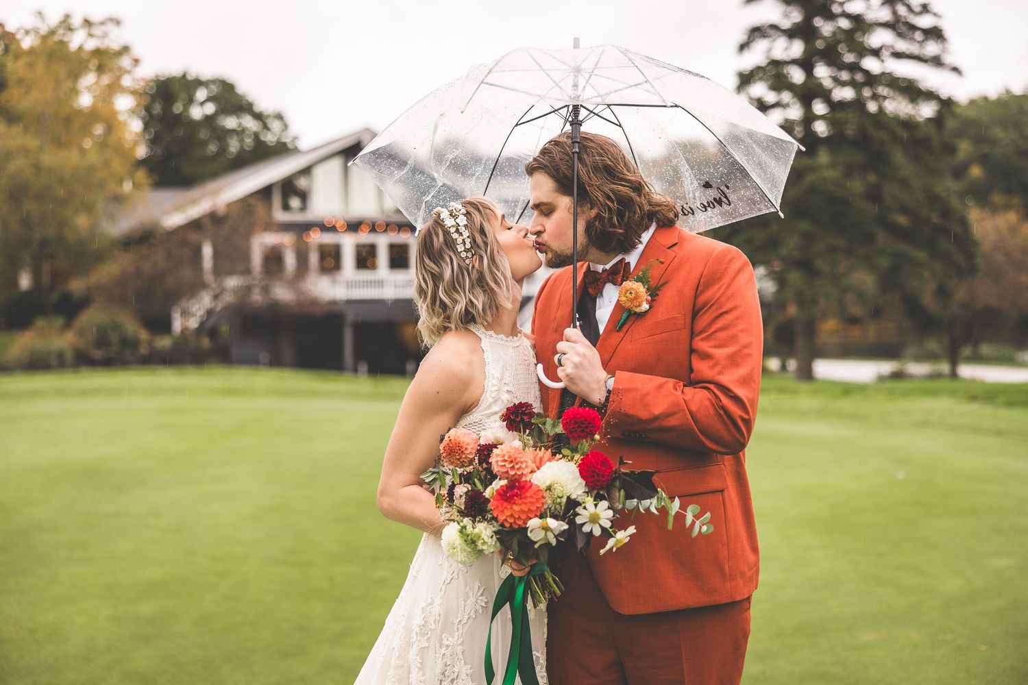 Intimate wedding moment captured under clear umbrella with autumn backdrop.