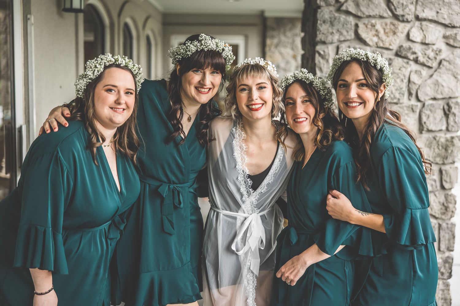 Wedding party wearing teal dresses poses together against stone wall.