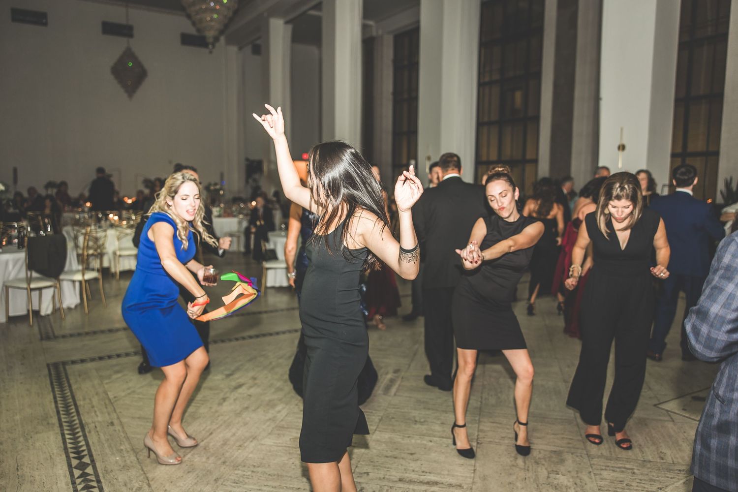 Wedding reception guests dance and celebrate in an elegant columned ballroom space.