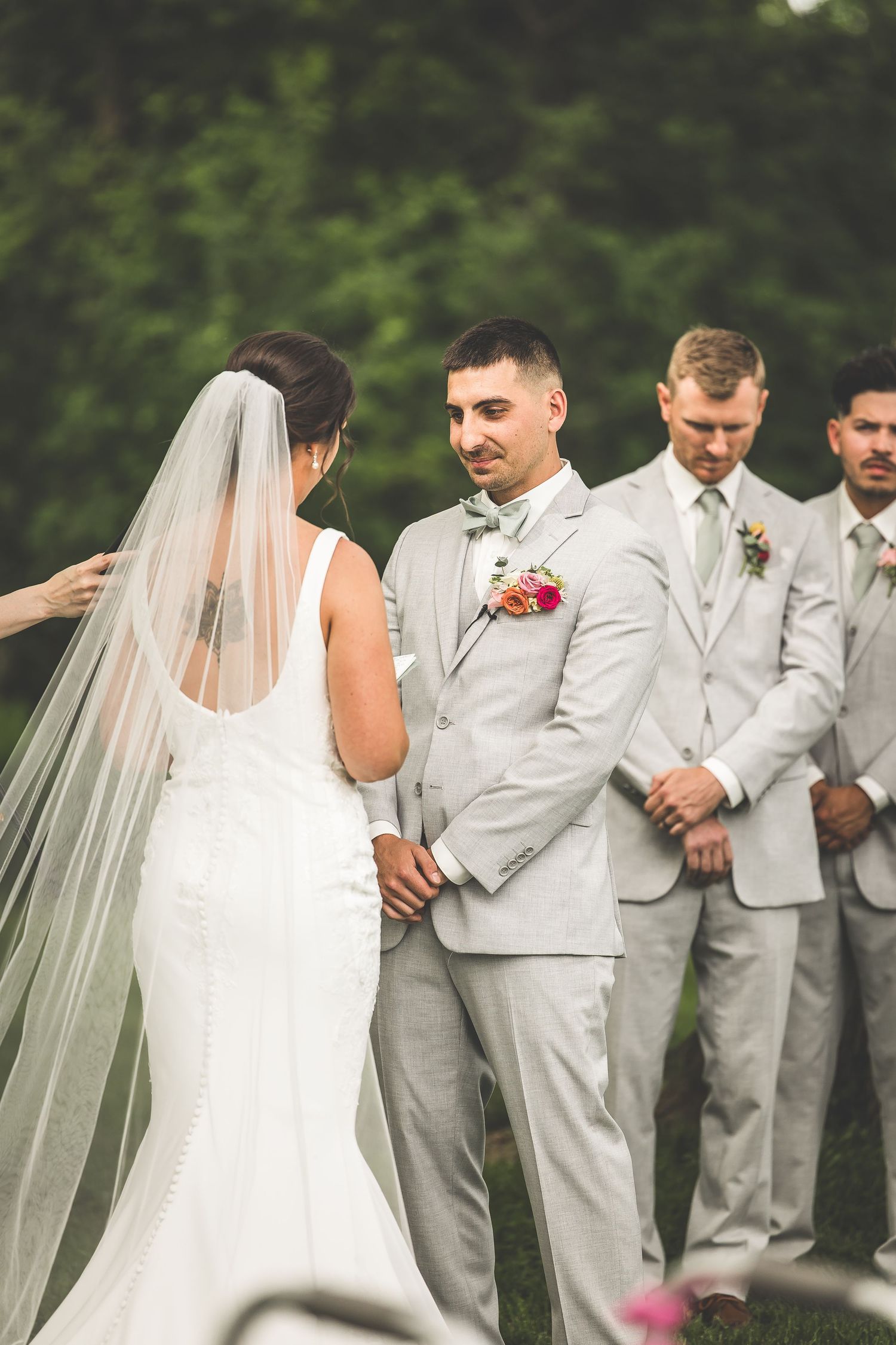 Intimate outdoor wedding ceremony with wedding party in light gray suits.