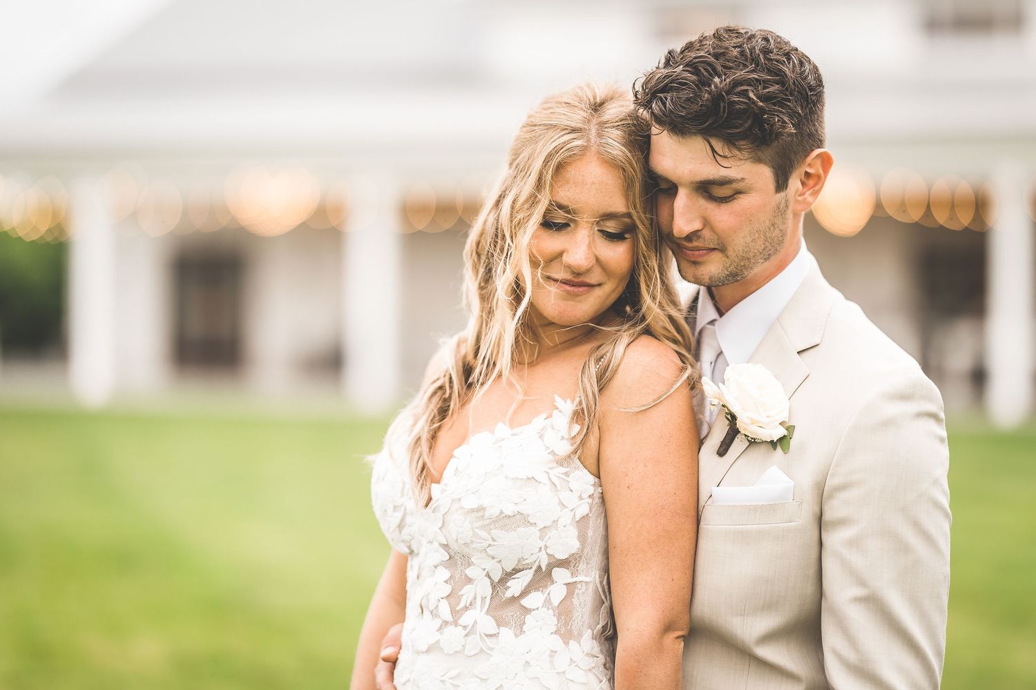 Romantic wedding portraits against a white farmhouse with string lights and rustic charm.