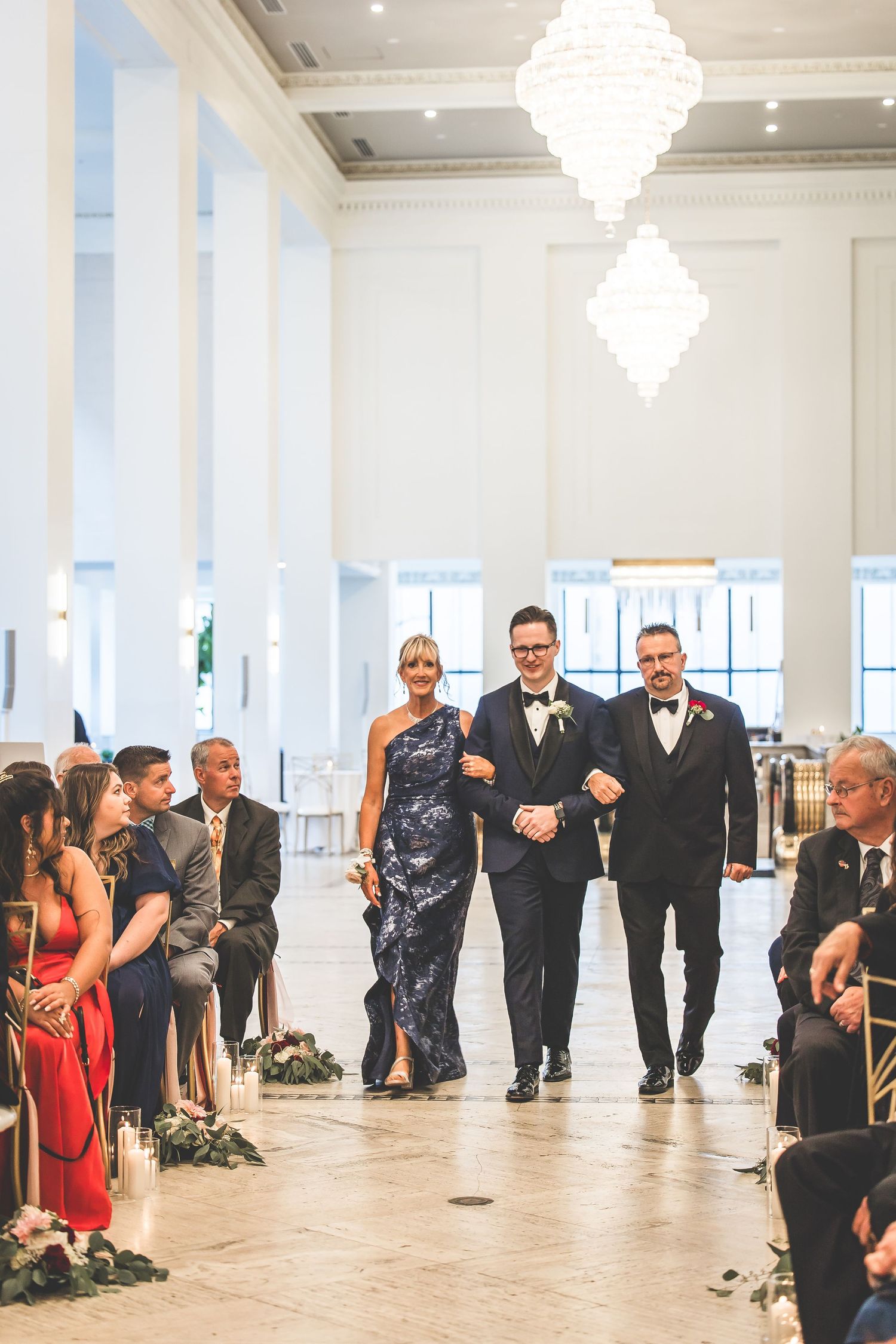 Wedding guests mingling in an elegant white ballroom under crystal chandeliers.