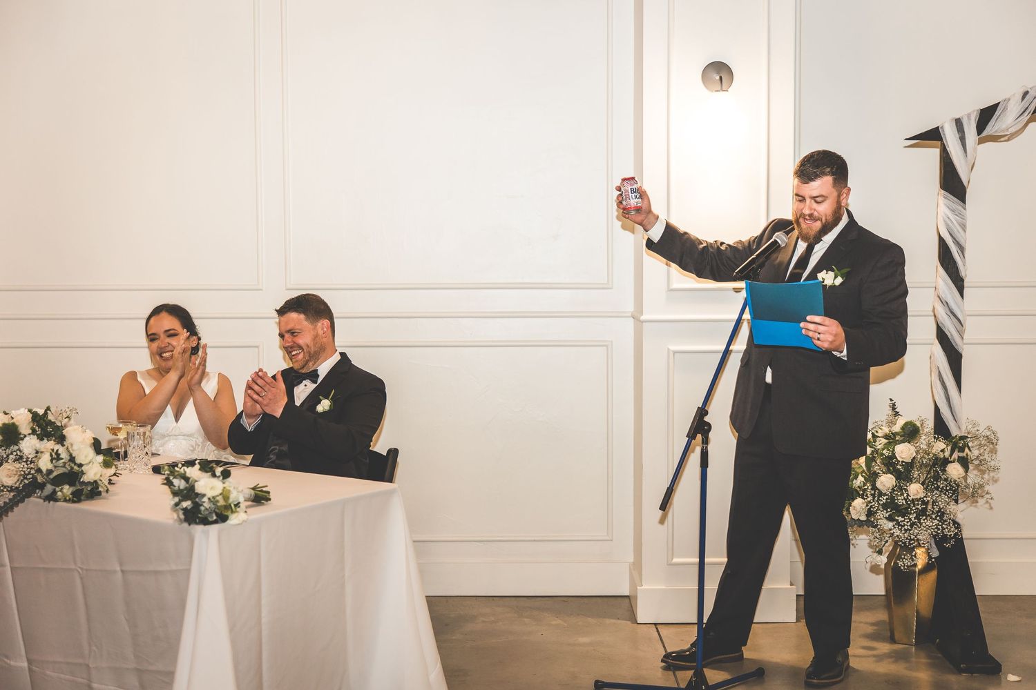 A wedding toast being given at the reception while the couple listens from their table.