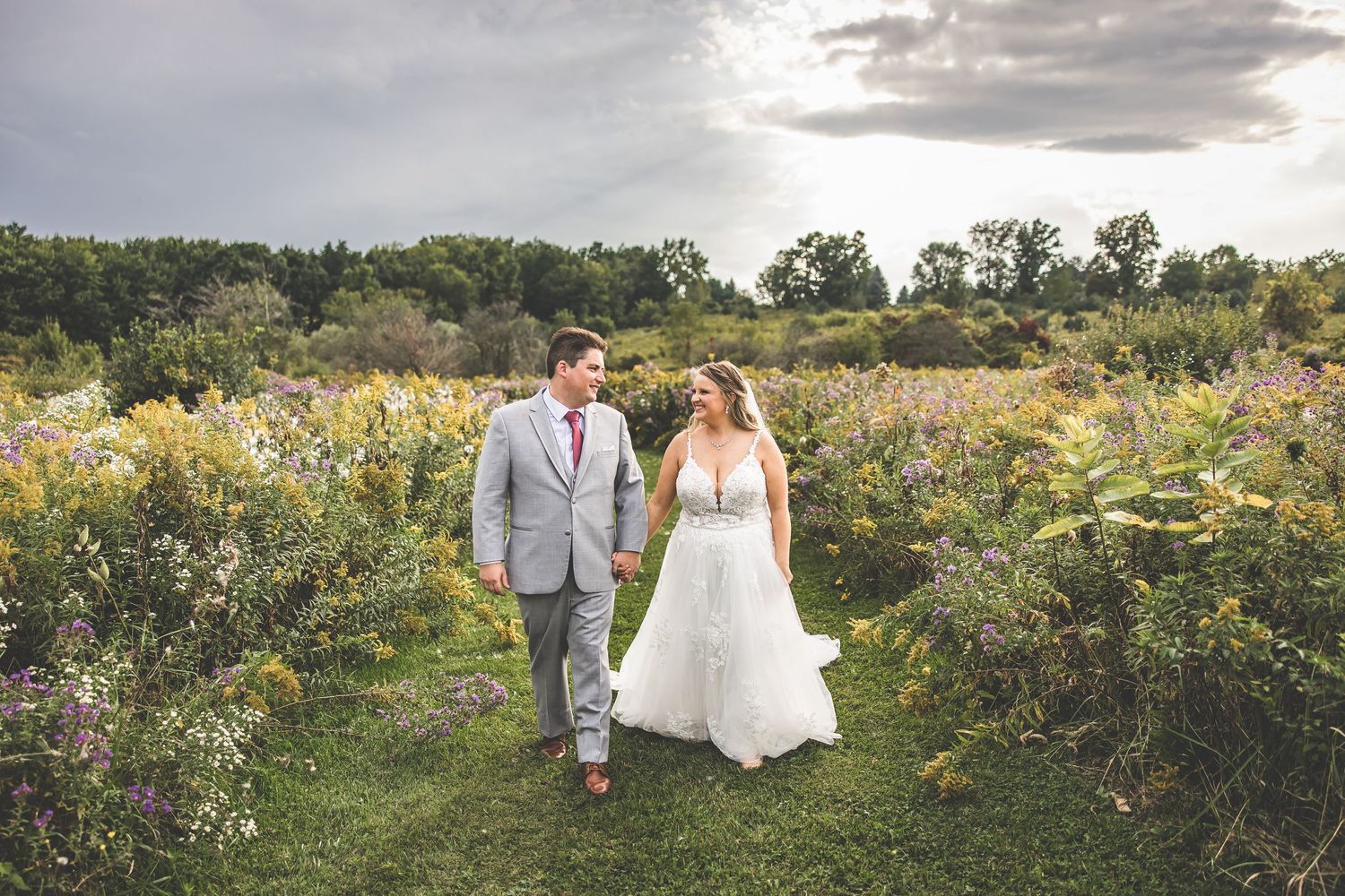A wedding couple walks hand in hand through a scenic garden filled with colorful flowers.