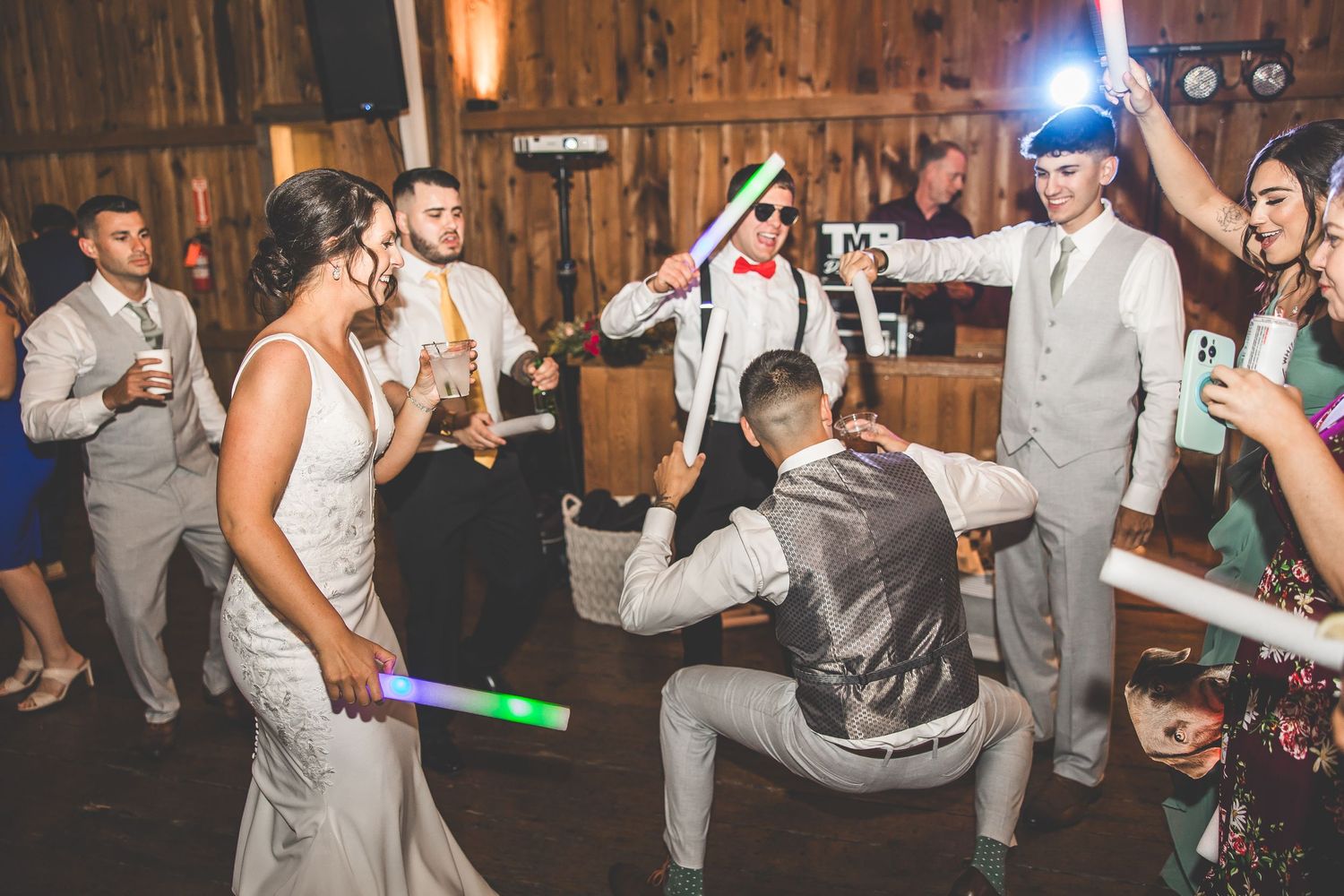 Wedding guests dancing with light-up props in a dimly lit barn venue.