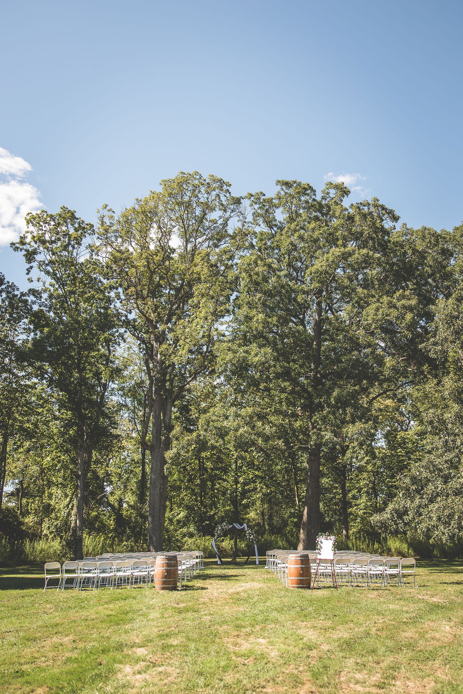 An outdoor wedding venue with rolling hills, tall trees, and wine barrels set up for a ceremony.