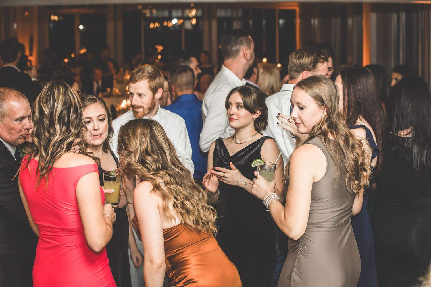 Wedding guests in colorful dresses socializing and dancing at an evening reception.