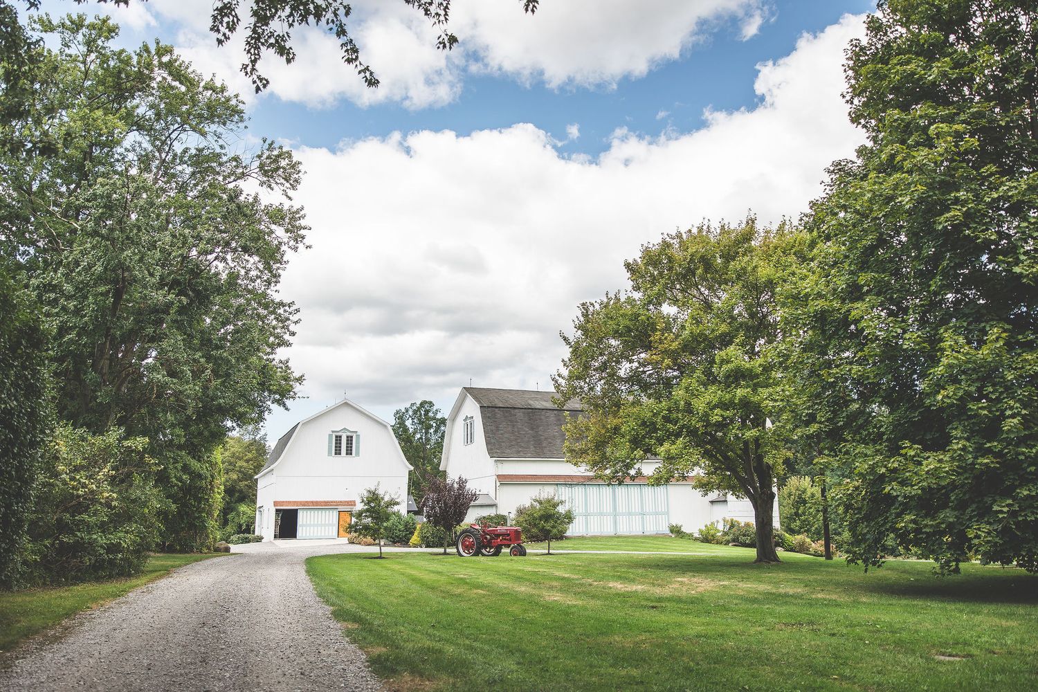 White farmhouse with green lawn and trees under cloudy summer sky.