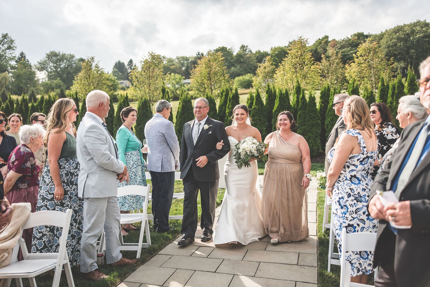 Outdoor wedding reception with guests gathered on stone patio surrounded by greenery.