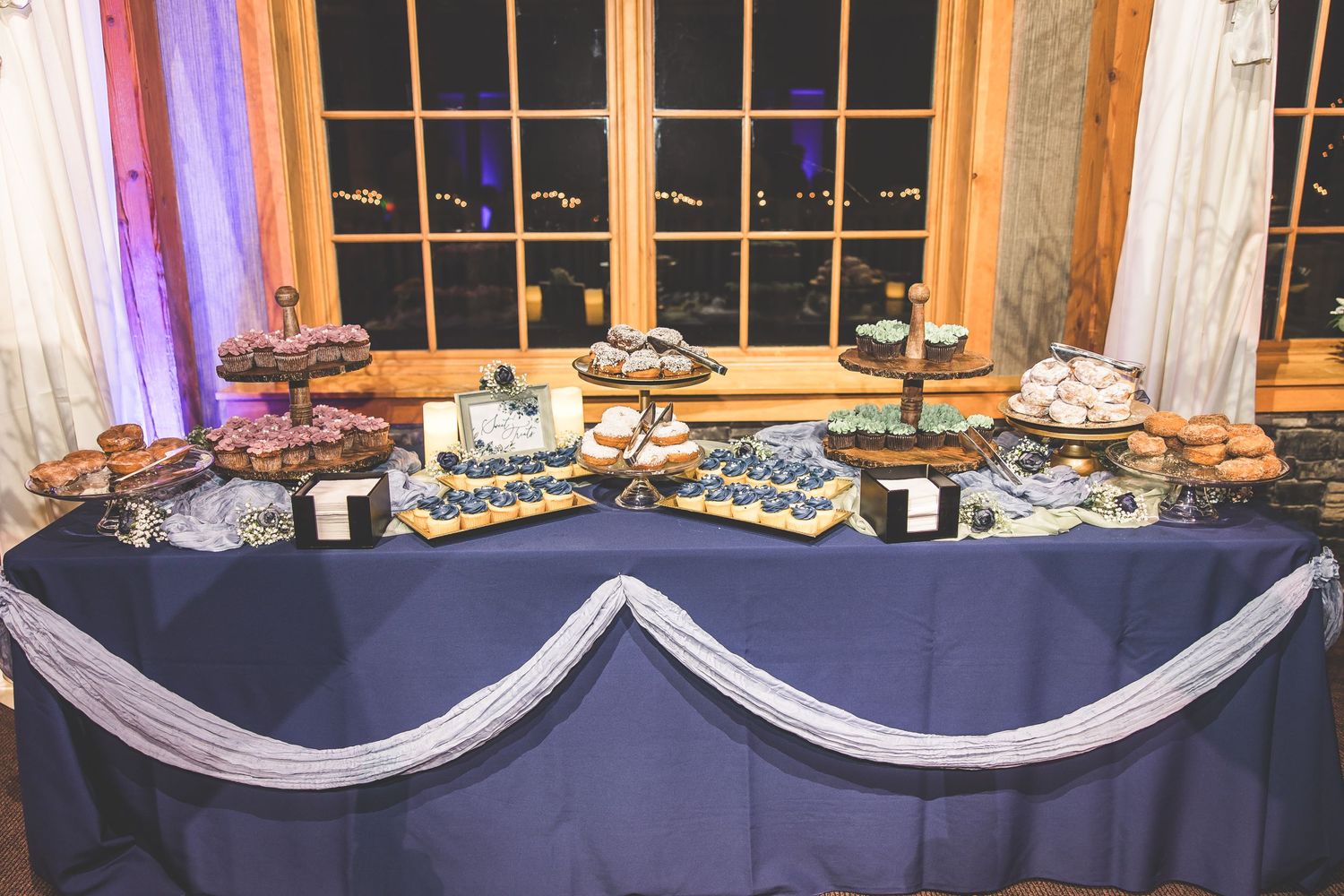 Elegant wedding reception buffet table setup with navy blue linens and white draping decor.