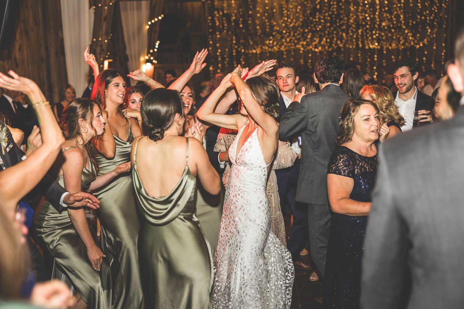 Wedding guests dancing and celebrating at reception with sparkly backdrop.