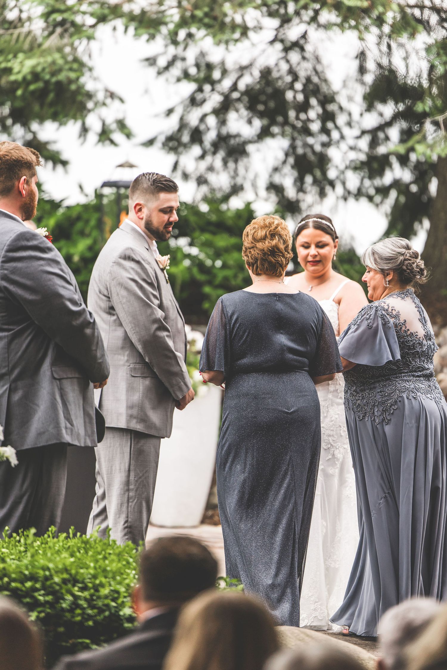 Wedding party in gray and blue attire mingles during outdoor celebration.