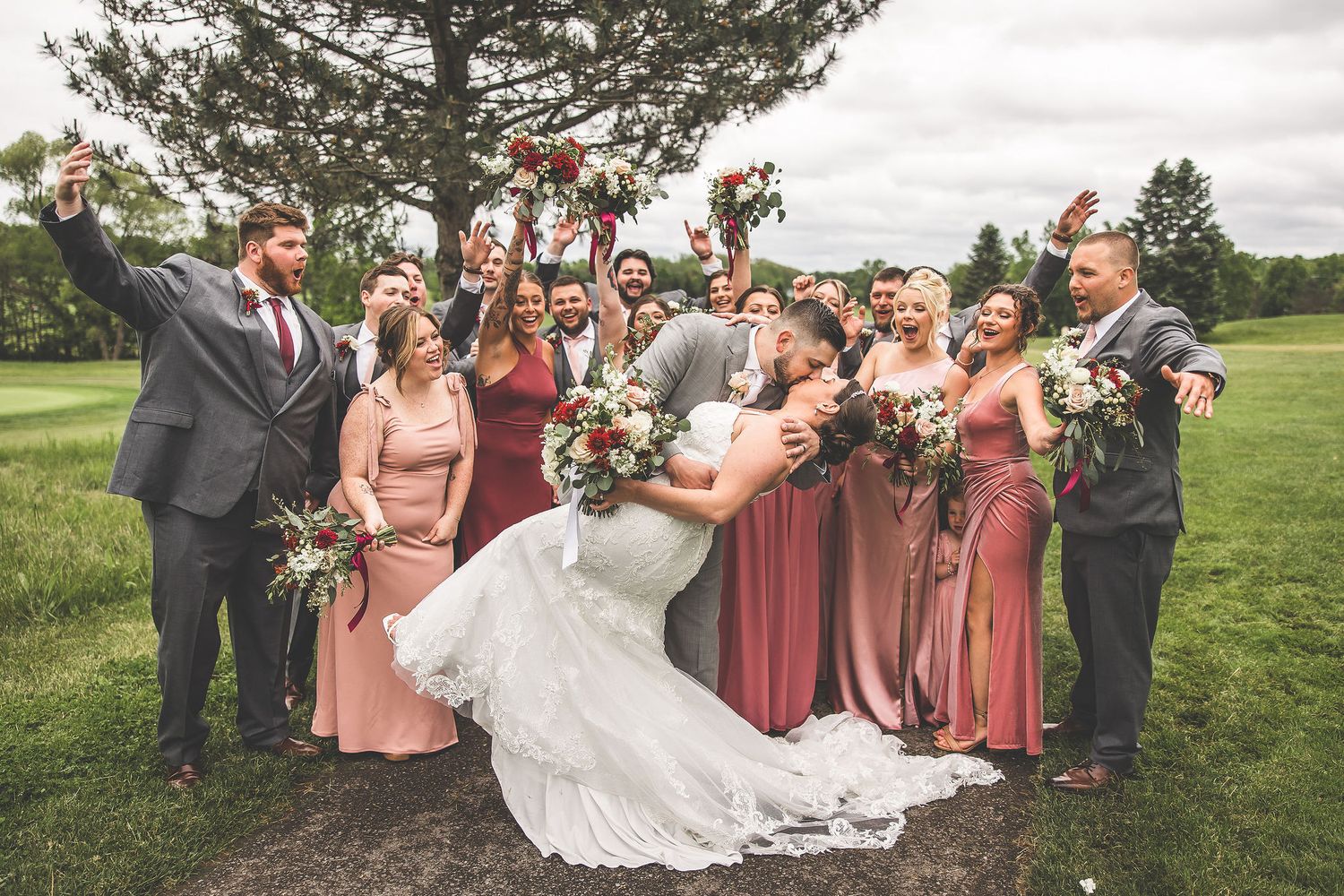 Wedding party poses for candid shots in pink dresses and gray suits on a golf course.
