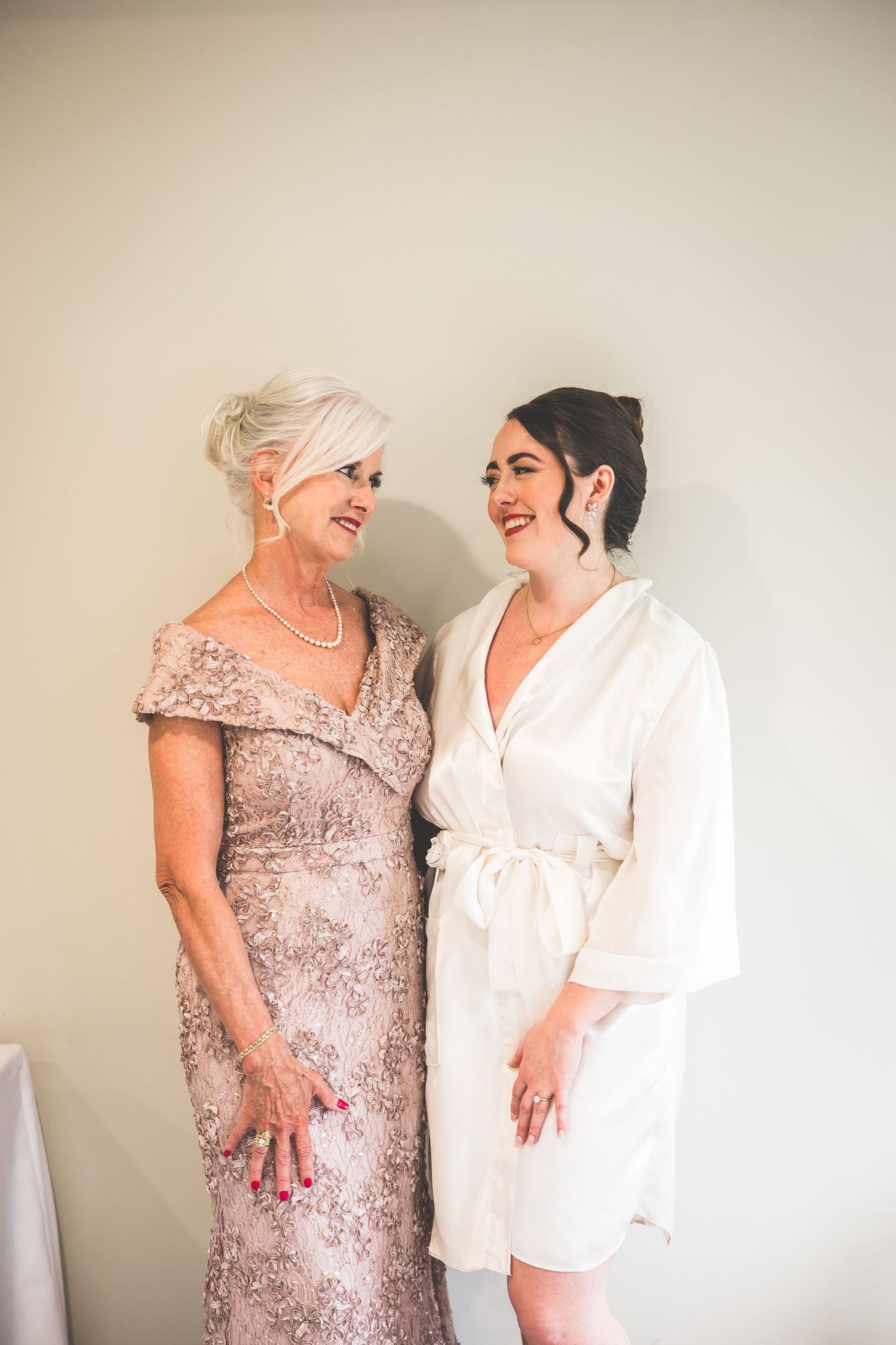 Two women sharing a joyful moment while getting ready in formal attire.