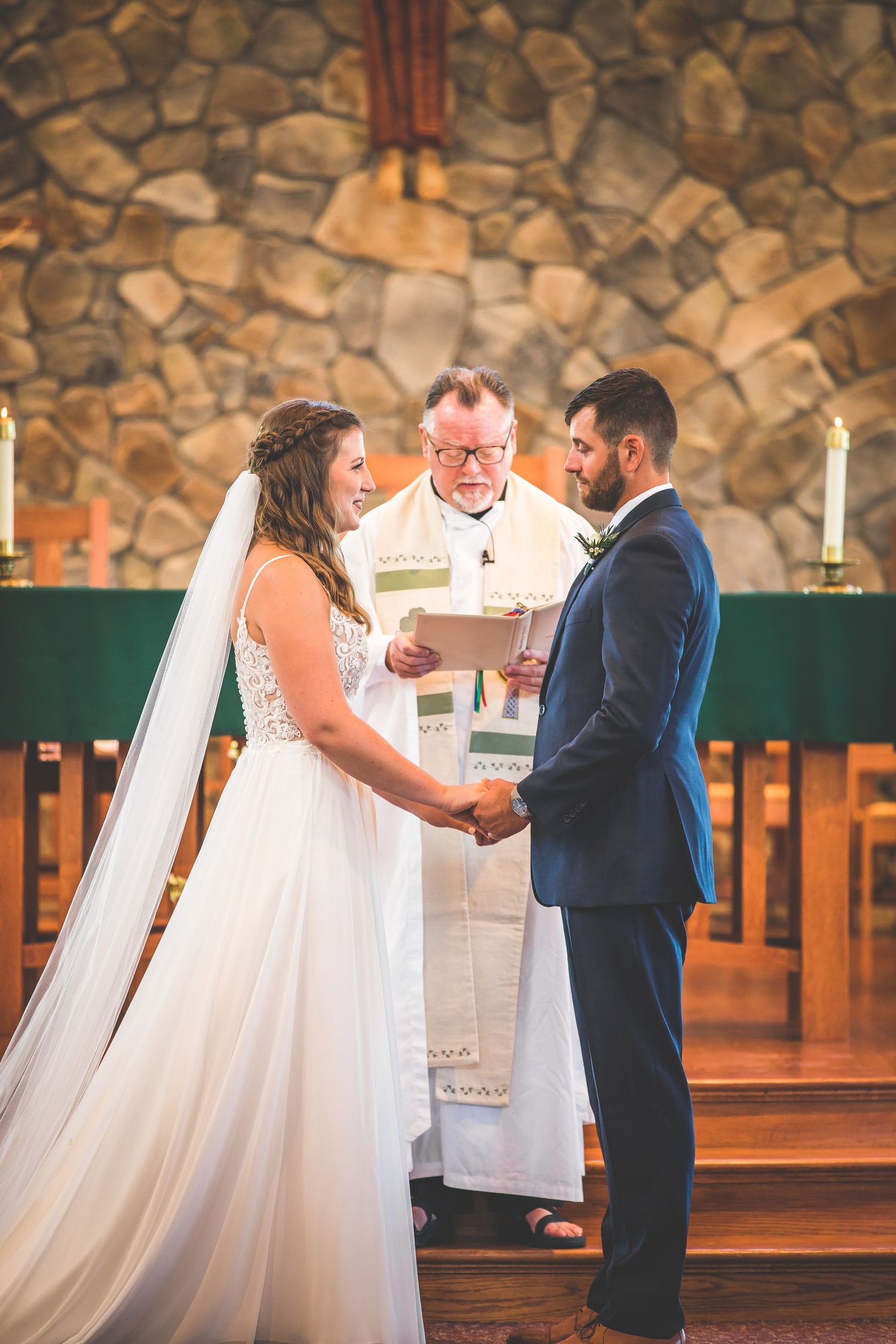 Wedding ceremony moments captured during ring exchange at stone-walled church altar.