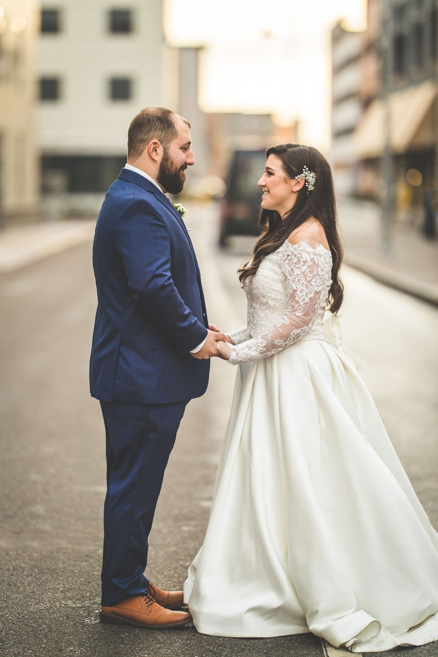 Wedding couple in blue suit and white dress pose together on urban street.