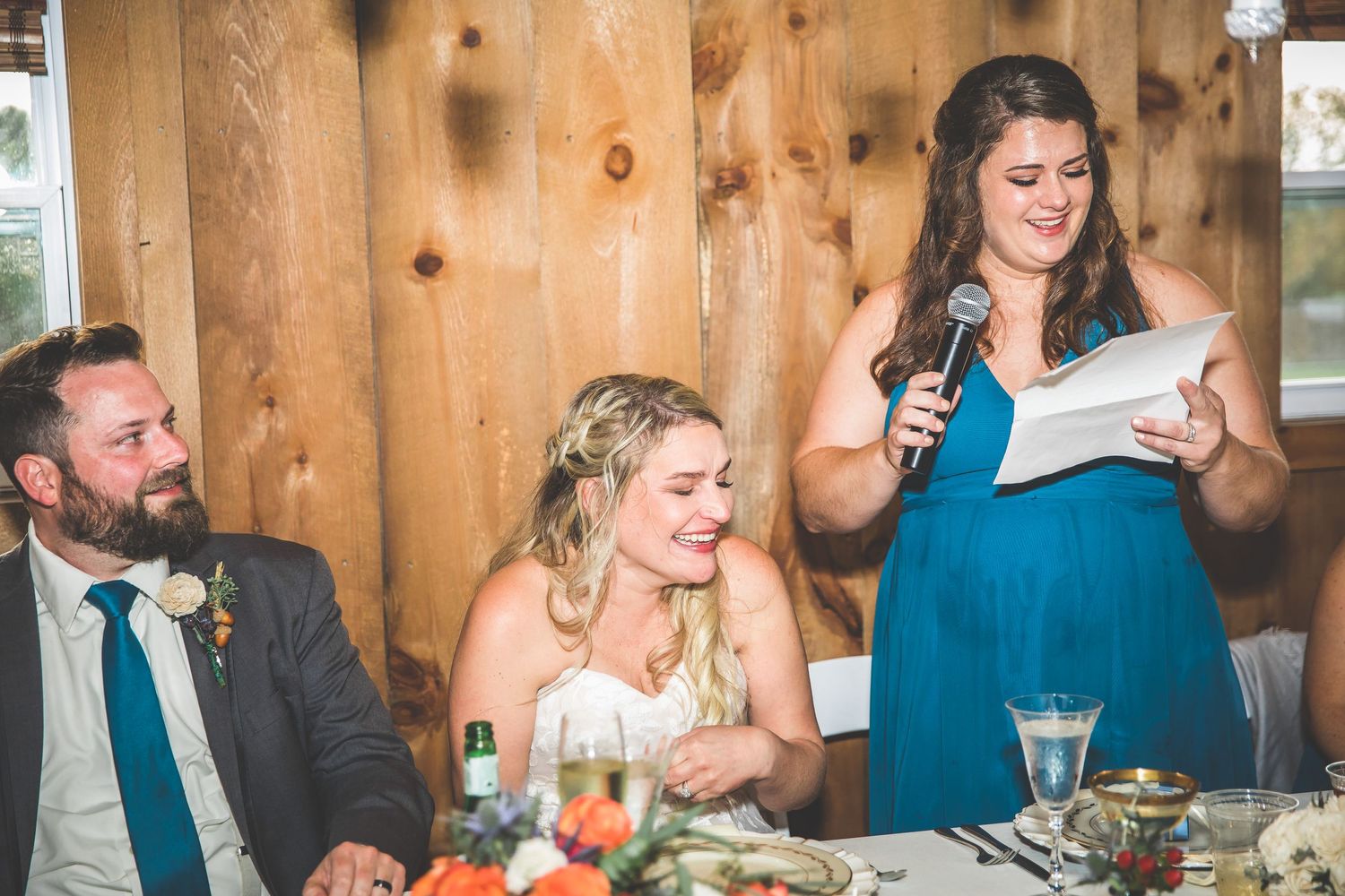 Wedding guests seated at long tables during reception in rustic barn setting.