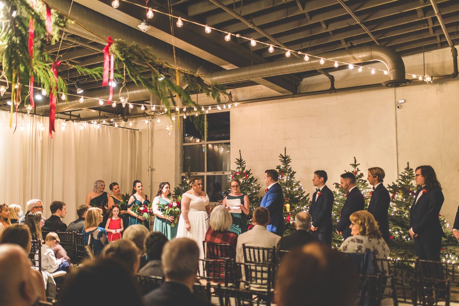 Wedding ceremony setup in an industrial venue with string lights and hanging greenery decorations.