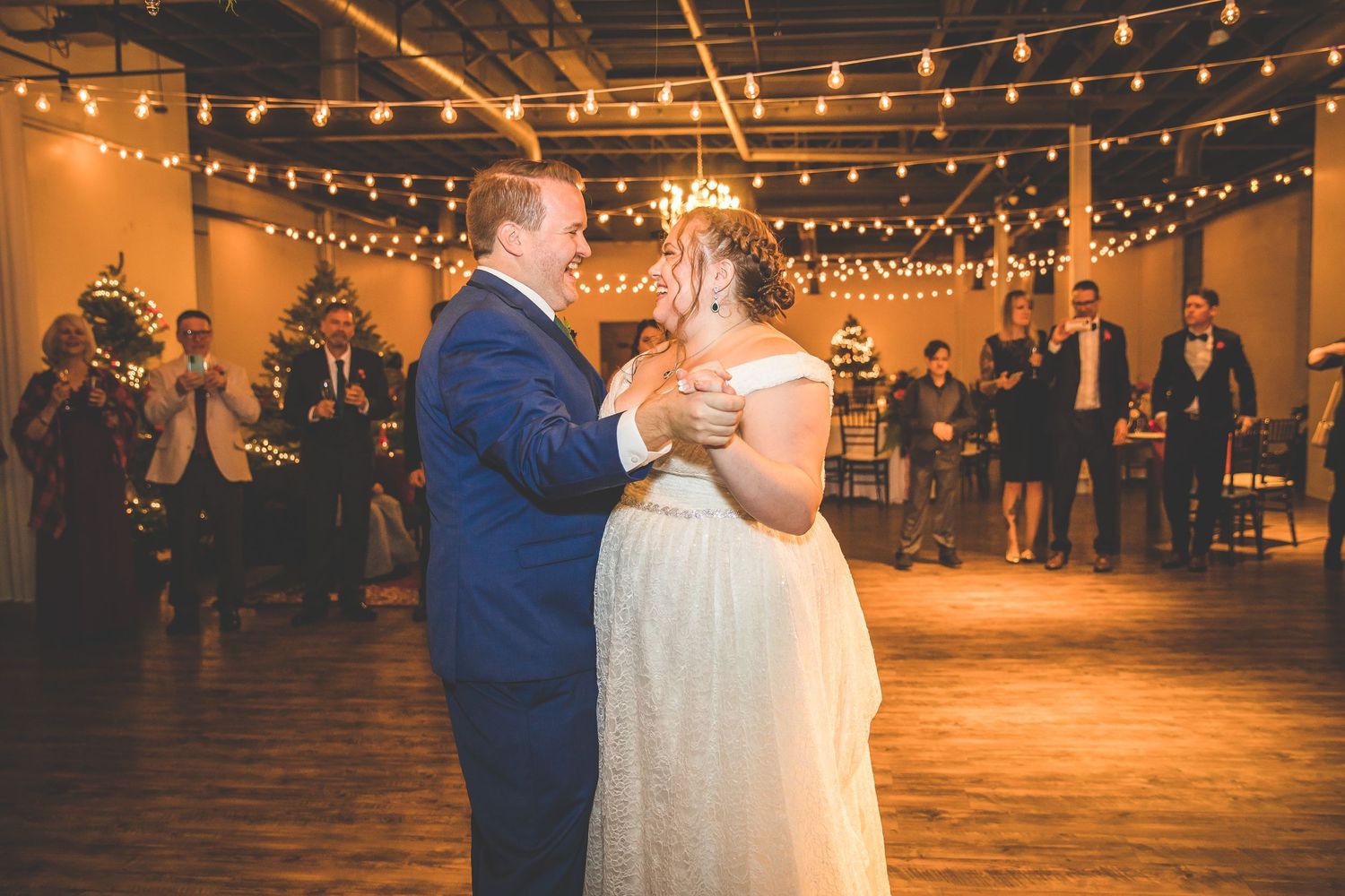 Couples dance under warm string lights at an indoor winter wedding reception.