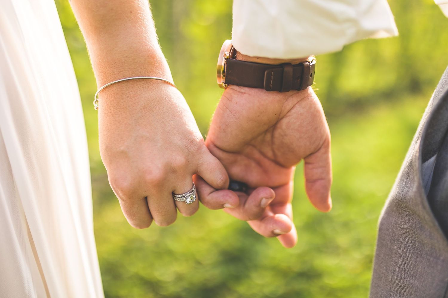 Close-up detail shots of hands and wedding attire in natural outdoor lighting.