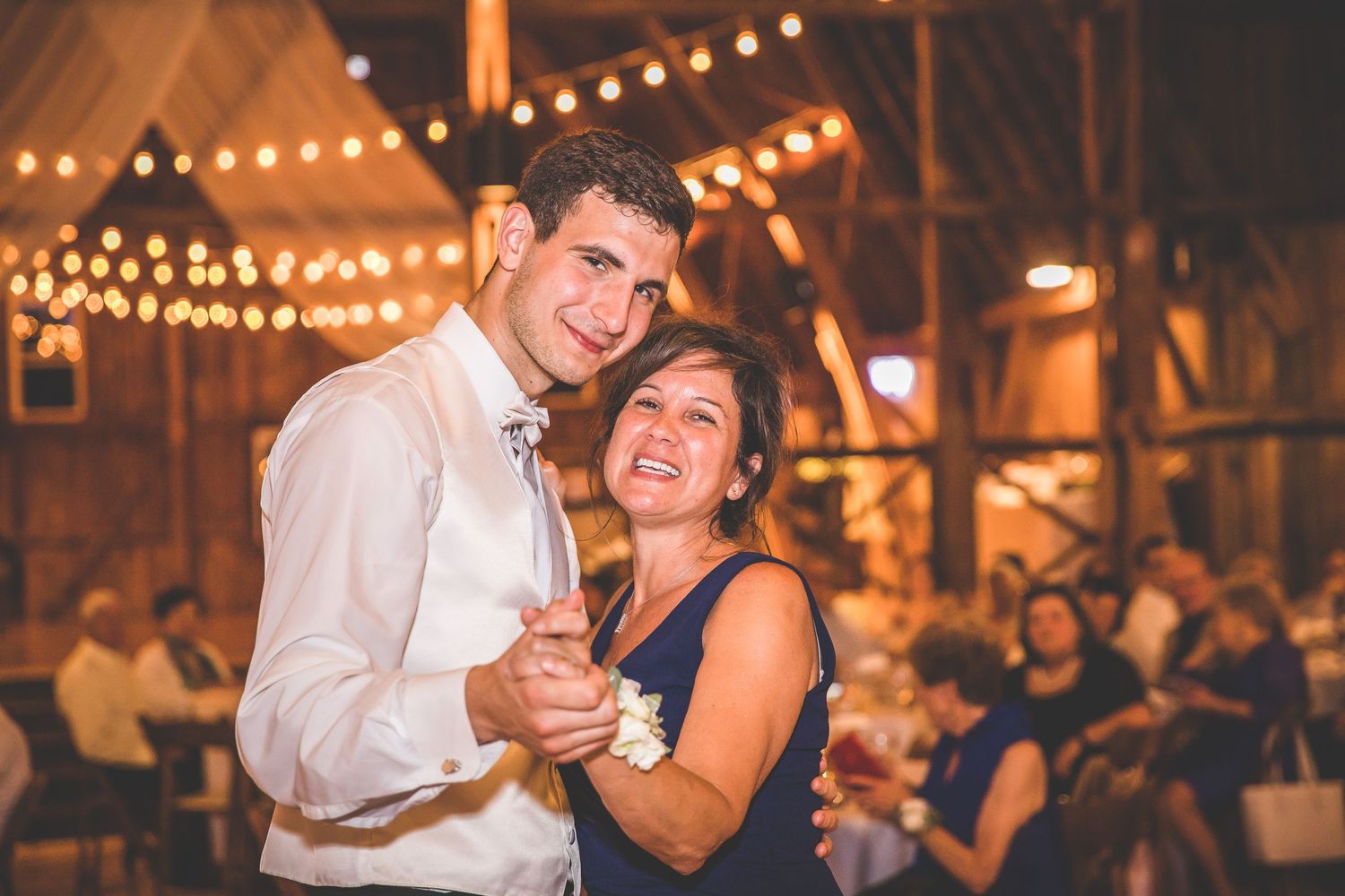 Couples dancing and laughing during a wedding reception in a warmly lit barn venue.