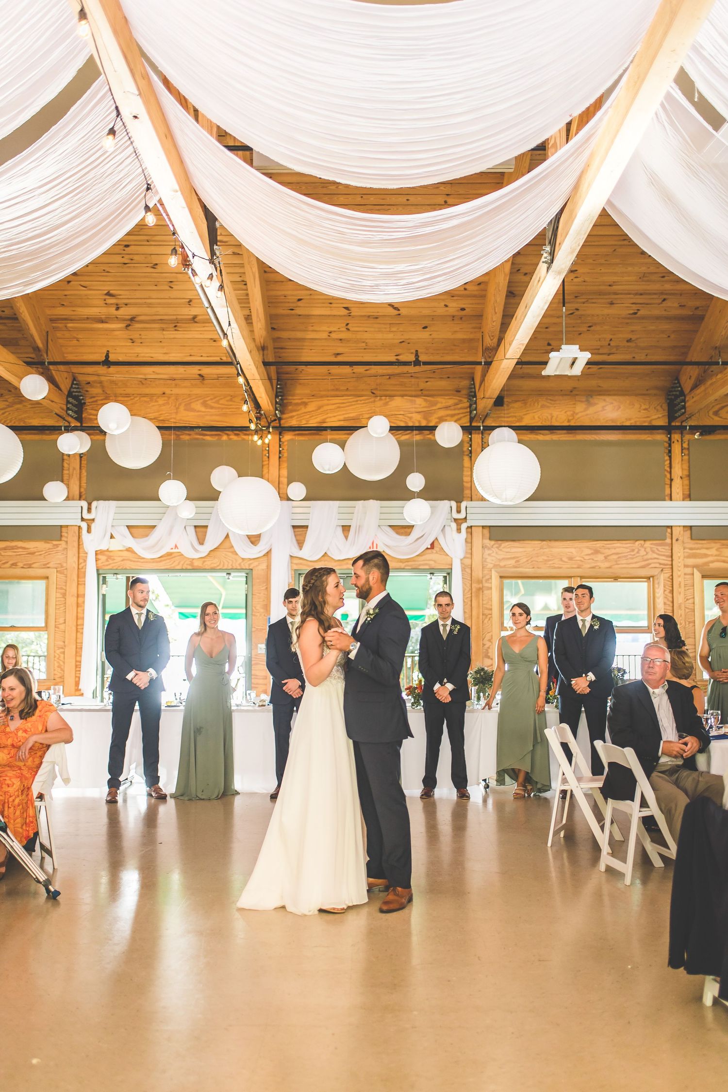 Elegant wedding ceremony setup with white fabric draping and paper lanterns in a wooden beam venue.