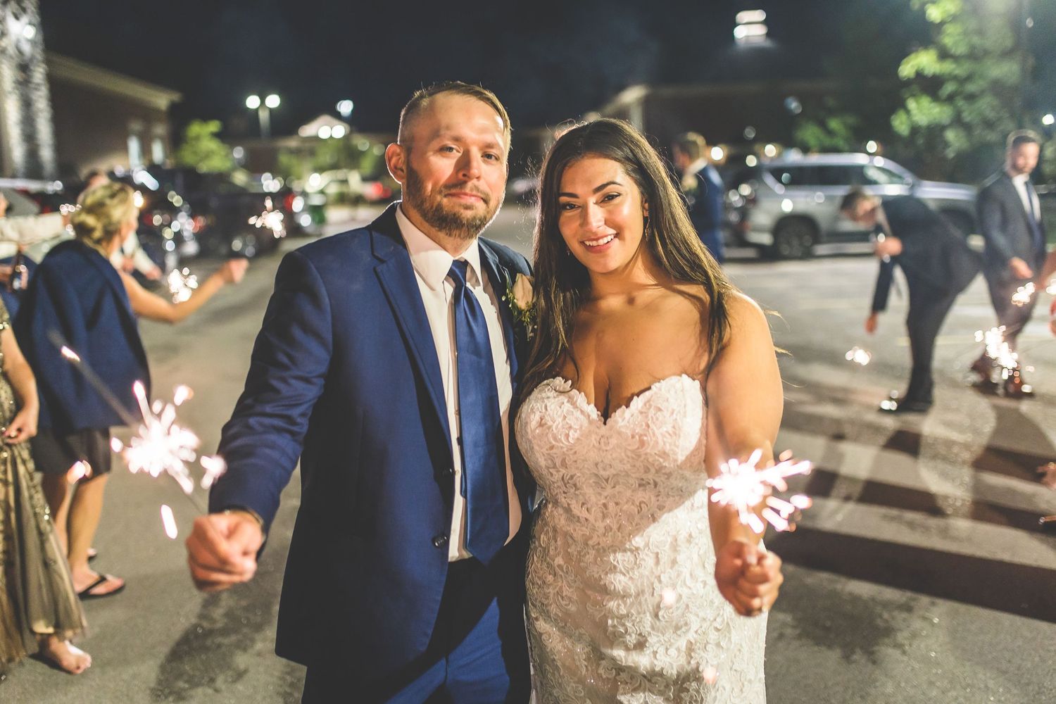 Newlyweds walking through sparkler exit with guests at night.