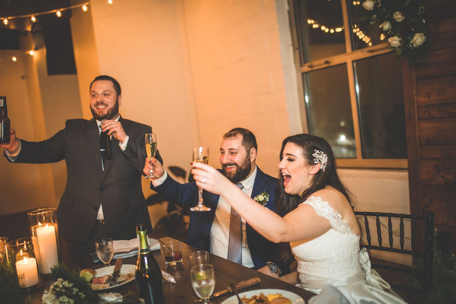 Wedding reception celebration with guests seated at tables decorated with string lights and candles.