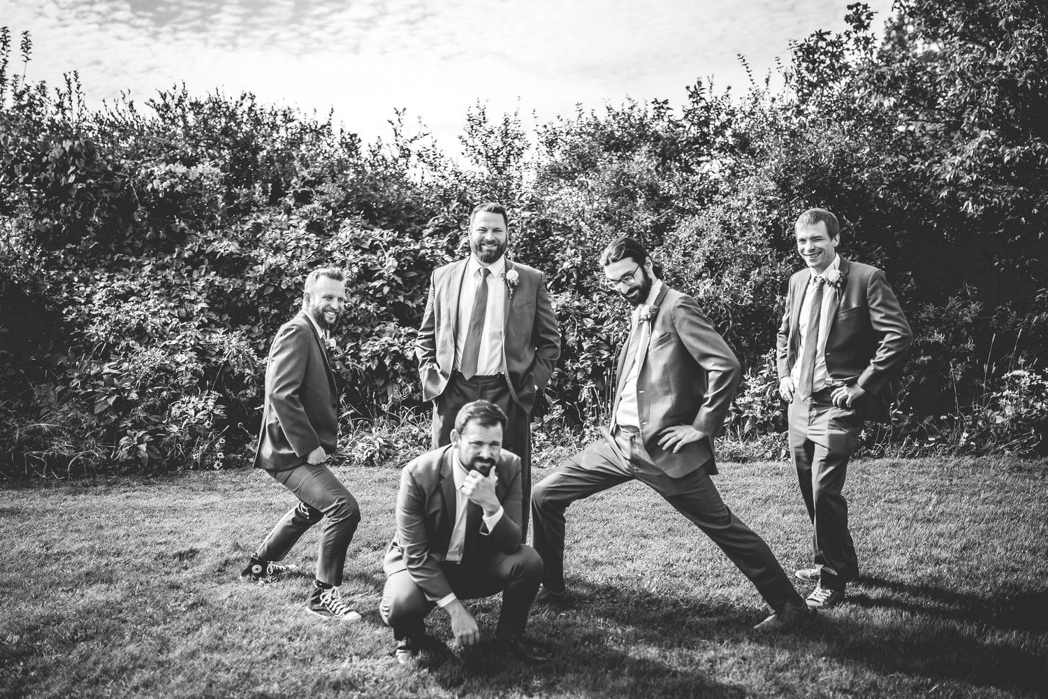 Black and white photo of wedding party having fun with playful poses in outdoor setting.