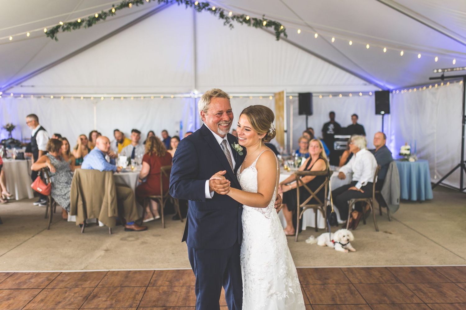 Wedding reception dance captured under elegant white tent with string lighting and floral decor.