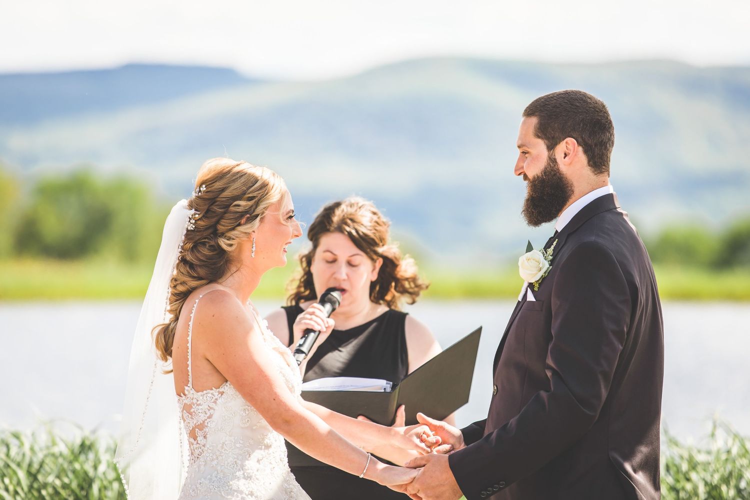 An emotional outdoor wedding ceremony takes place beside a serene lake with mountains in the background.