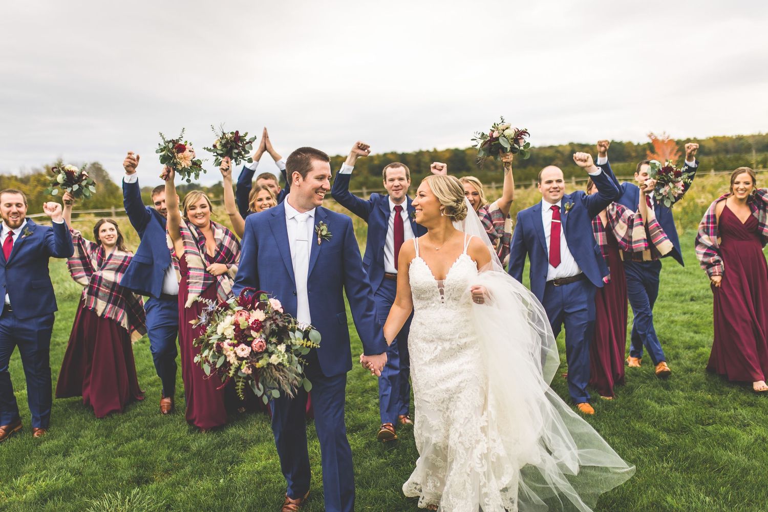 Large wedding party celebrates with the newlyweds in an outdoor field setting.