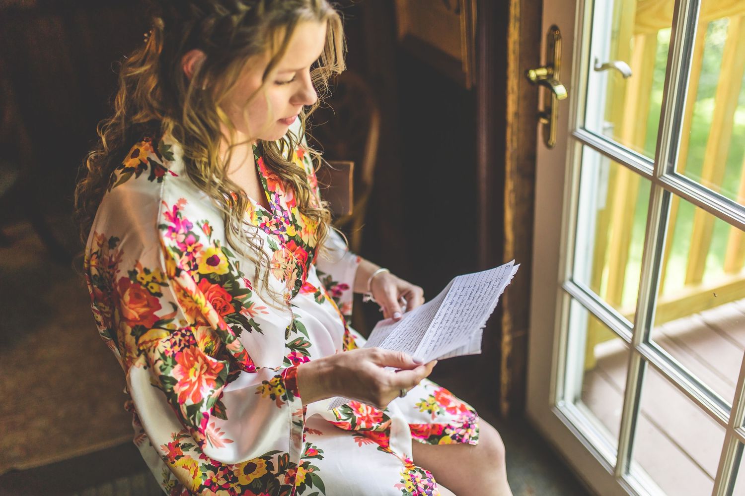 A floral robe being worn while reading a letter near a bright window.