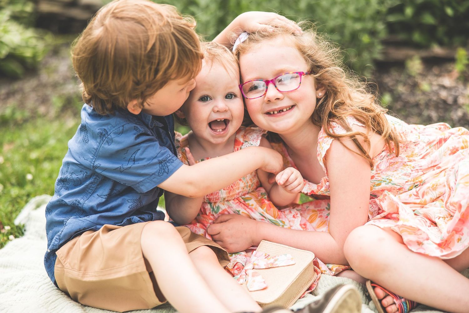 Family lying together on a blanket outdoors during a playful summer photo session.