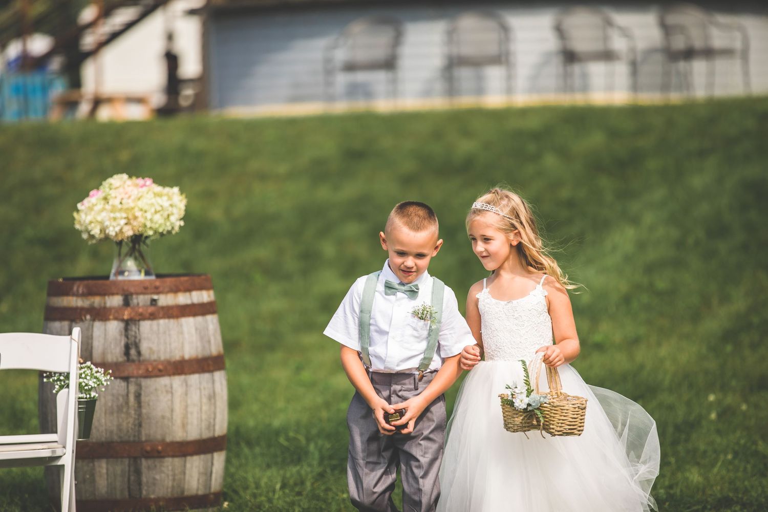 Young ring bearer and flower girl walking on grassy path at outdoor wedding.