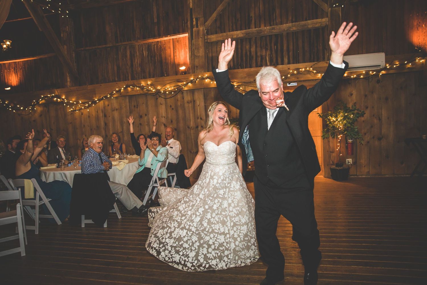 Elegant wedding reception dance in a rustic barn venue with warm lighting and string lights.
